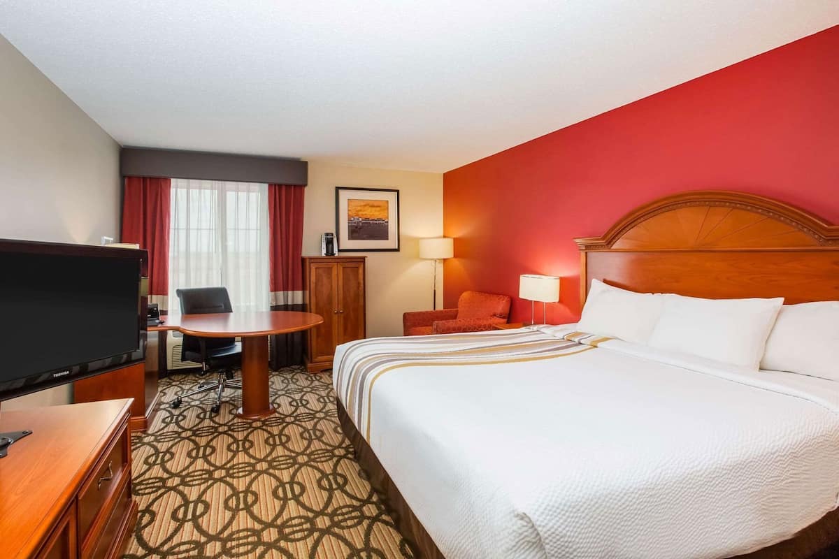 Ein Hotelzimmer mit Bett, Schreibtisch mit Fernseher, Stuhl, Tisch und Schrank.