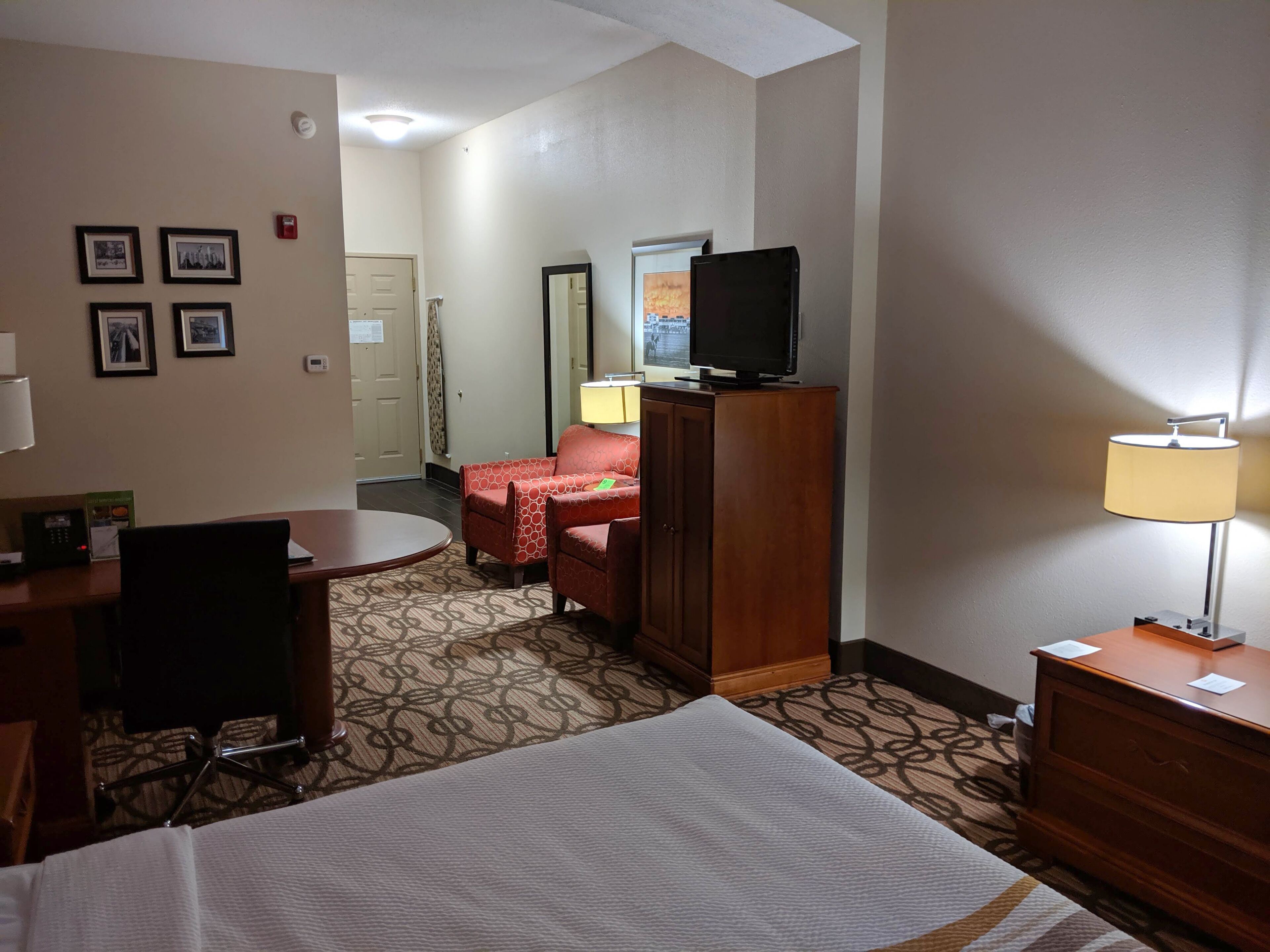 A hotel room with a bed, a desk with a chair, a red sofa, a television on a cabinet, and a lamp.
