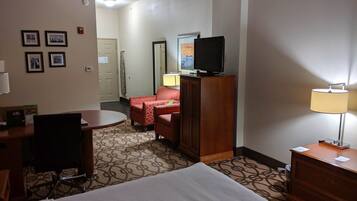 Una habitación de hotel con una cama, un escritorio con una silla, un sofá rojo, un televisor sobre un mueble y una lámpara.