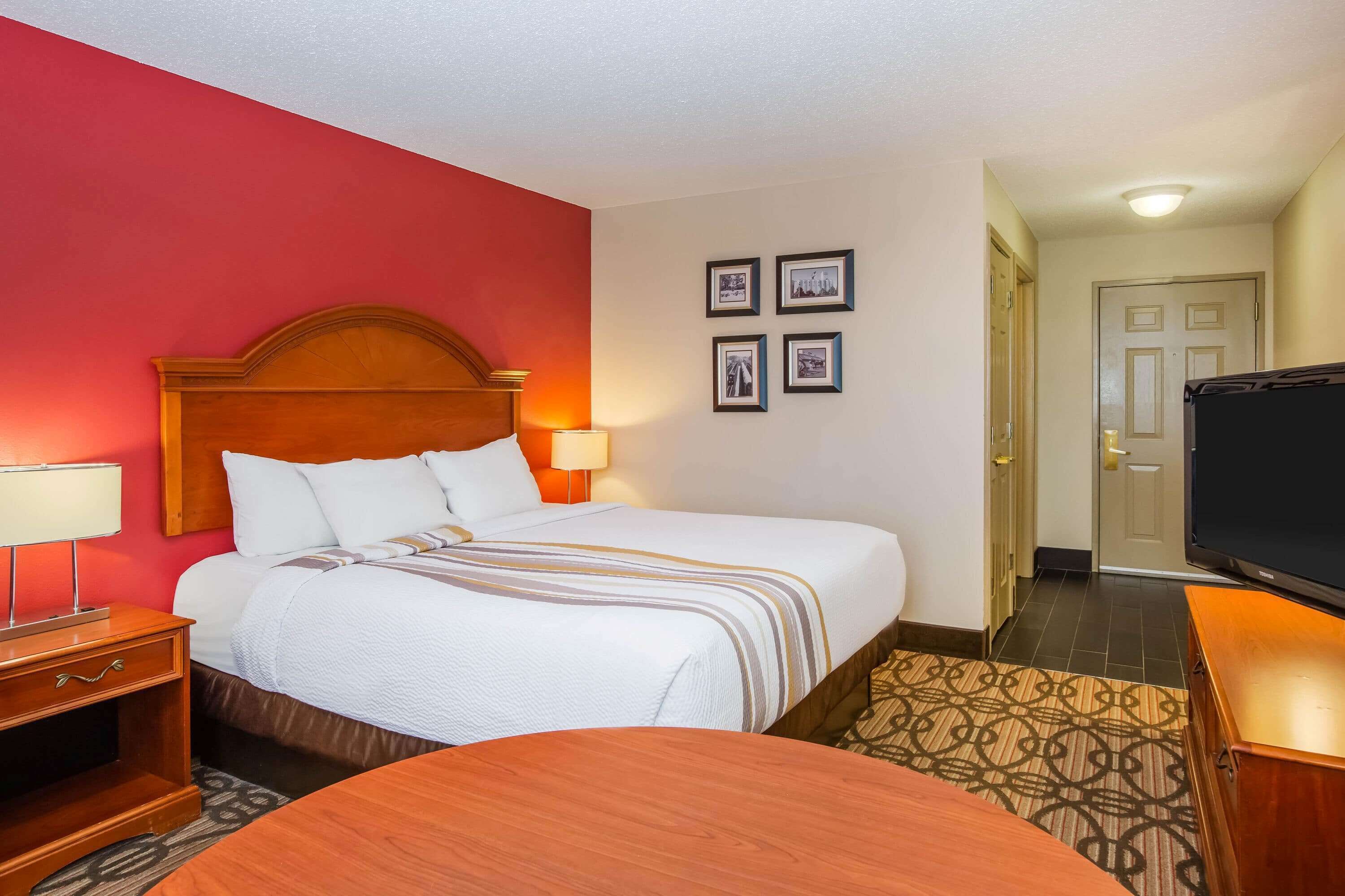 A hotel room with a large bed, a wooden nightstand, a TV, and a patterned rug.