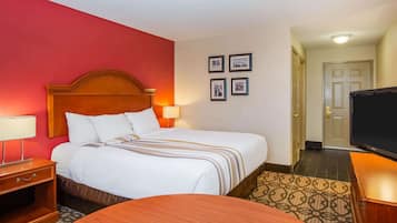 A hotel room with a large bed, a wooden nightstand, a TV, and a patterned rug.