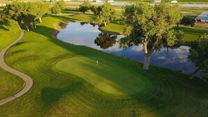 Un campo de golf con un estanque, árboles y un sendero.