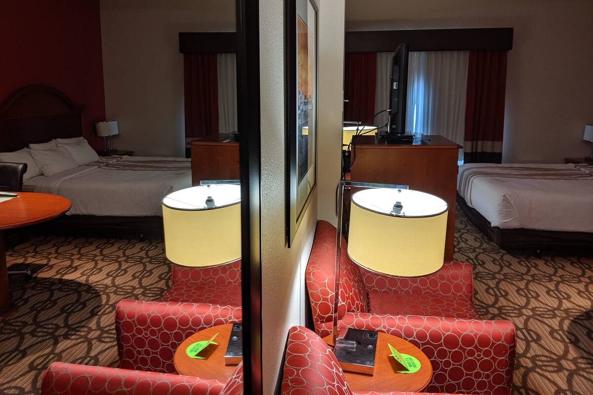 Ein Hotelzimmer mit zwei Betten, einem Schreibtisch, einem Stuhl und einem Spiegel.