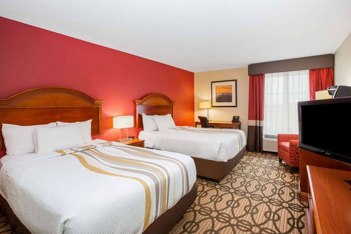 Een hotelkamer met twee bedden, een bureau, een stoel, een televisie en een raam met gordijnen.