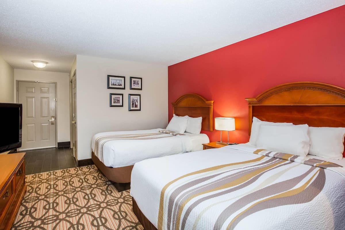 Ein Hotelzimmer mit zwei Betten, einem Fernseher, einer Tür und gerahmten Bildern an der Wand.
