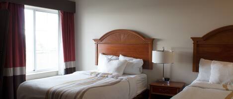 A hotel room with two beds, a nightstand with a lamp, and a window with curtains.