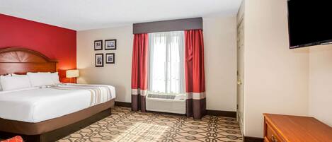 Habitación de hotel con cama, pared roja, ventana con cortinas rojas, televisor de pantalla plana y alfombra estampada.