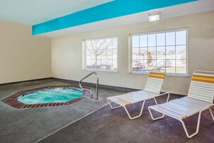 Una piscina interior con borde de ladrillo, dos tumbonas y vistas al exterior a través de ventanas.