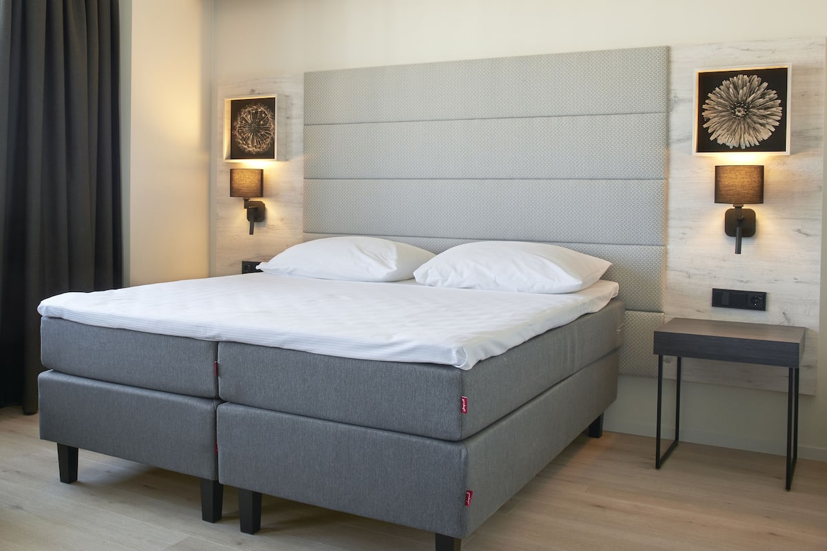 Een moderne slaapkamer met een grijze slaapbank, twee wandlampen en een kleine tafel.