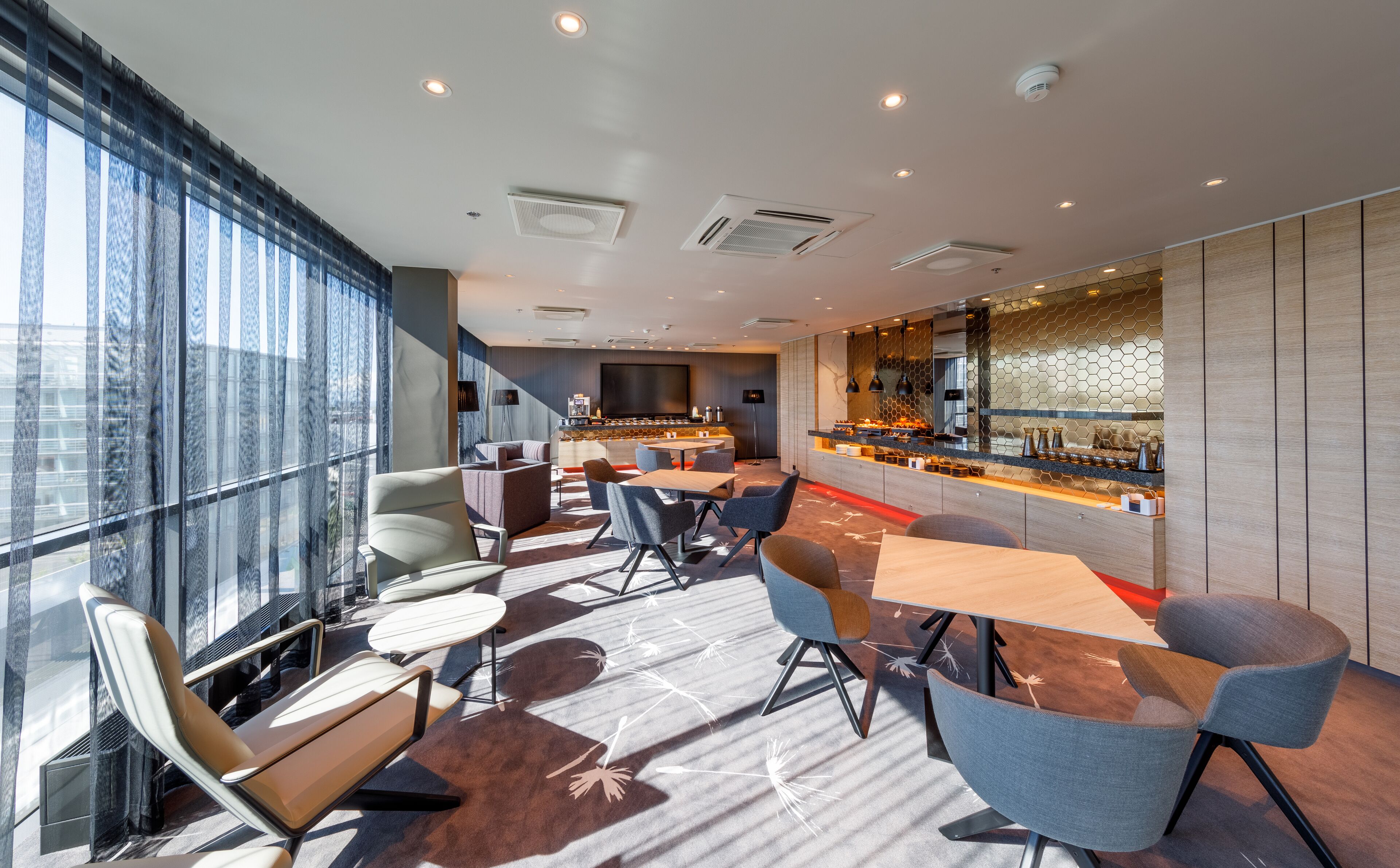 Un hall d’hôtel moderne doté d’un bar, de différents espaces de détente et d’un grand écran.