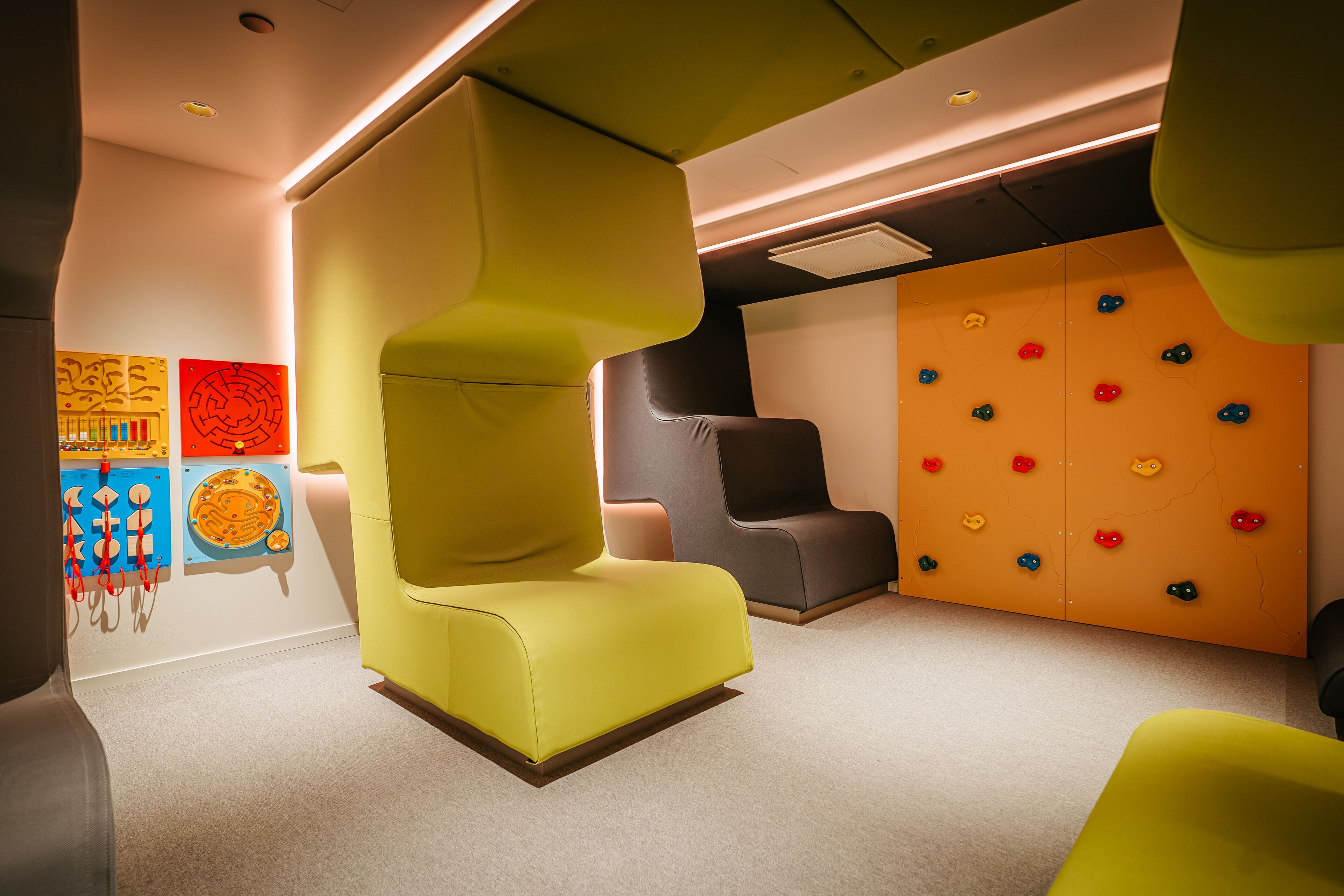 A modern interior with a yellow armchair, a climbing wall, and abstract art on the wall.