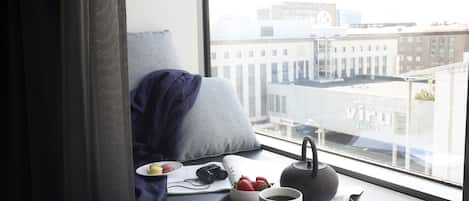A breakfast setup on a windowsill with a cup of coffee, a teapot, a bowl of strawberries, a plate with macarons, and a camera on a magazine.