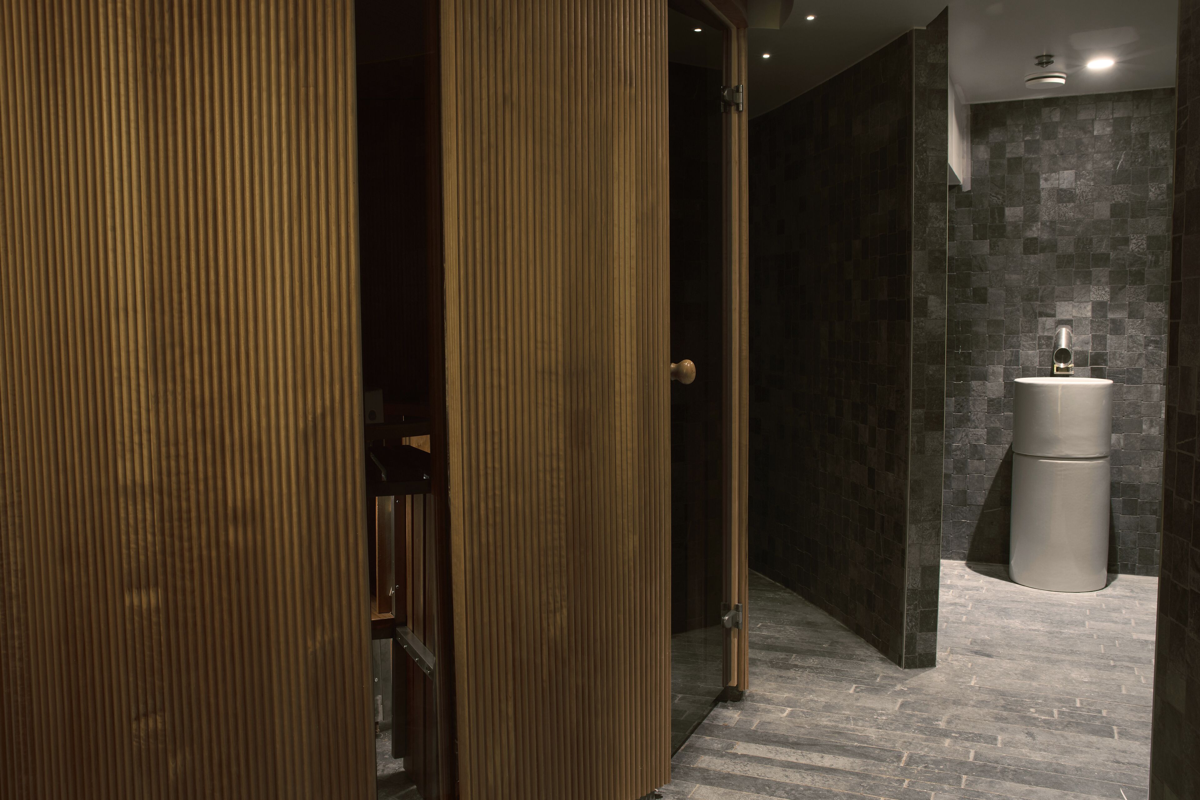 A modern bathroom with a wooden door, a sink, and a tiled wall.