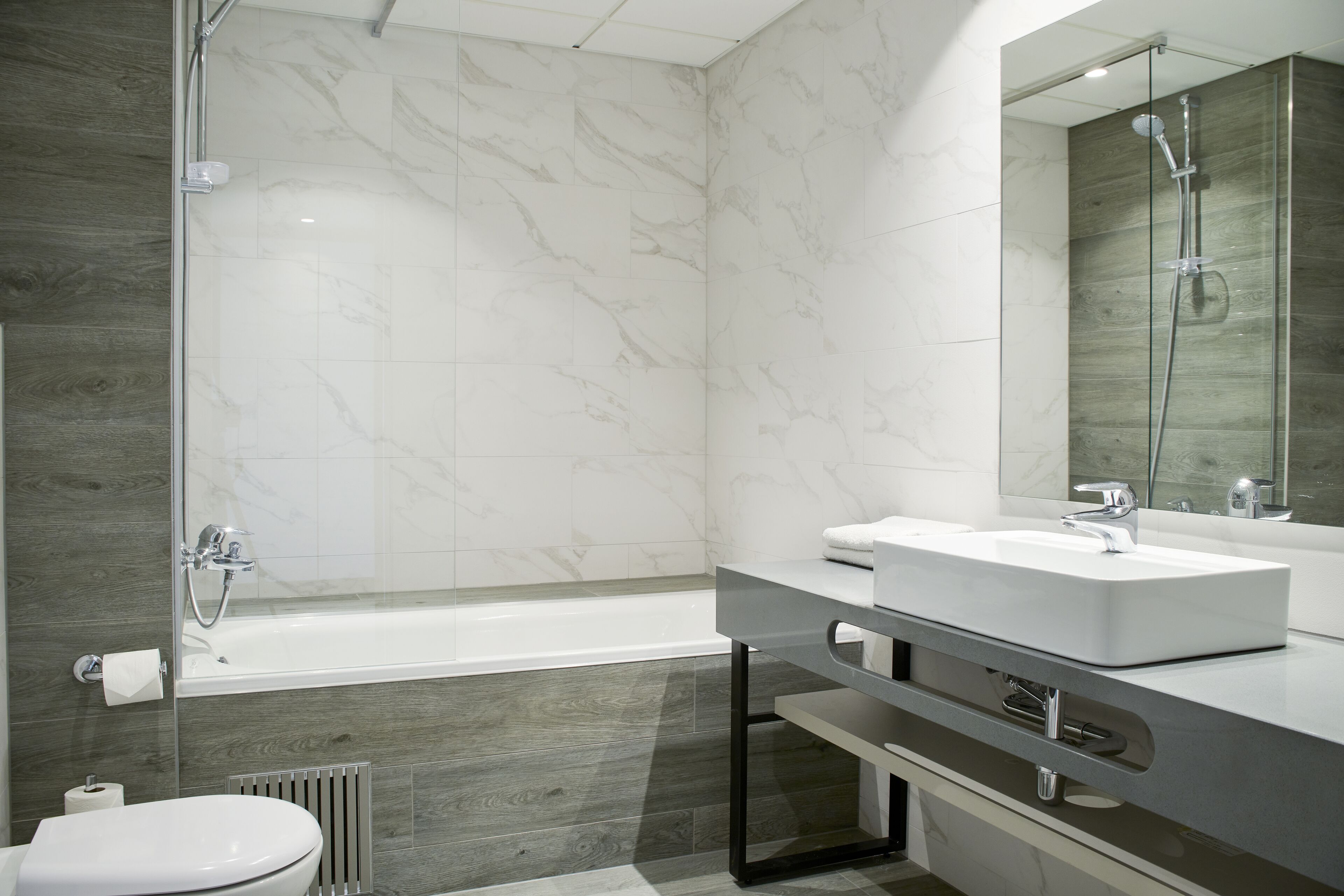 A modern bathroom with a bathtub, a vanity with a mirror, and a toilet.