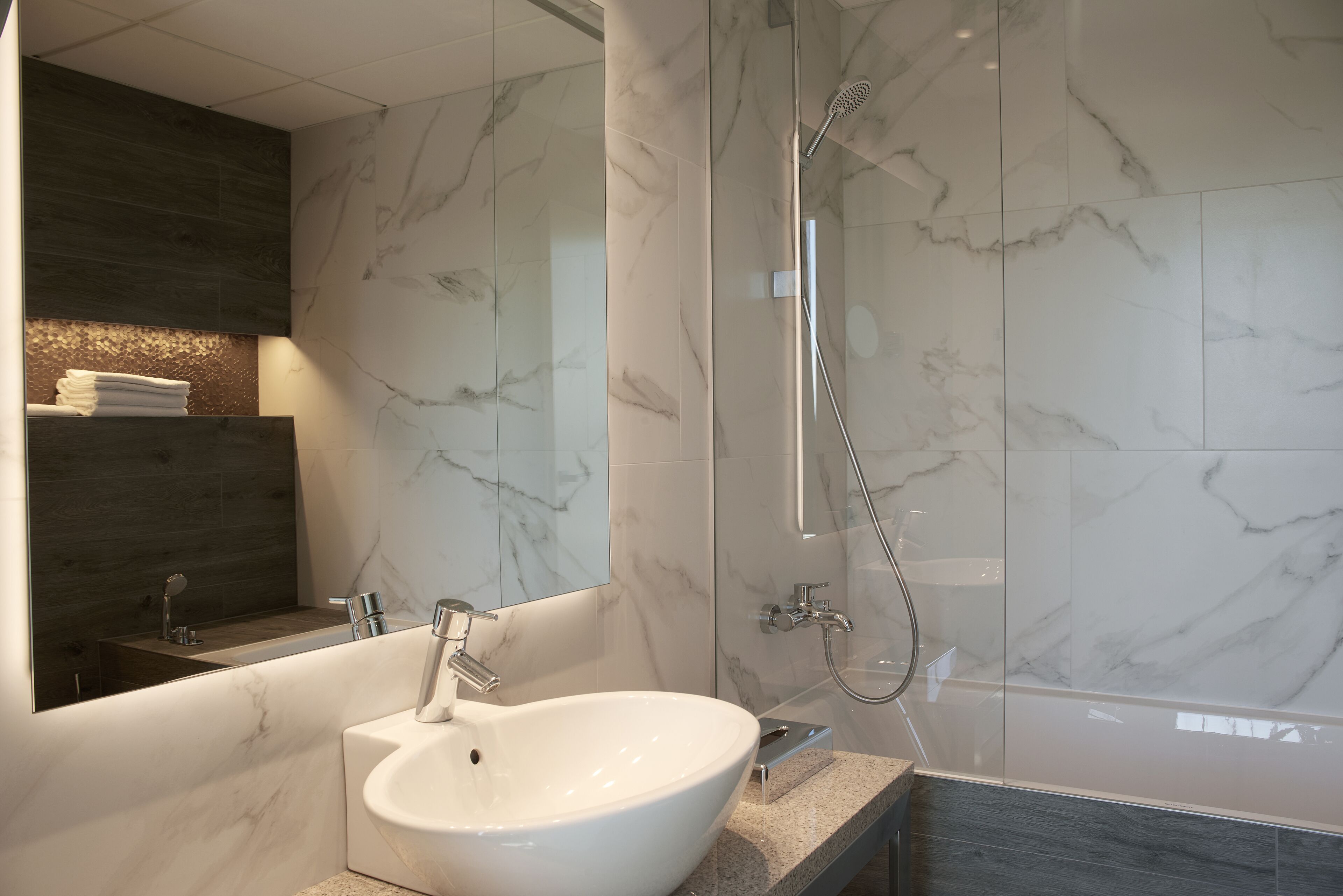 Un baño moderno con un lavamanos grande blanco, un espejo y una zona de ducha.