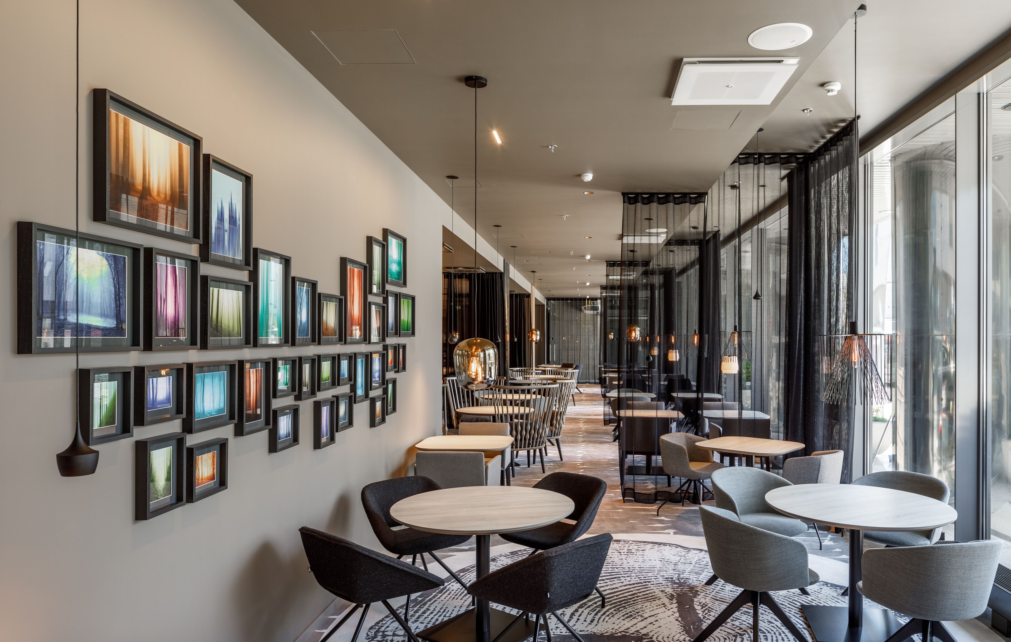 A modern interior with framed artwork on the walls, a variety of seating arrangements, and large windows providing natural light.