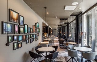 A modern interior with framed artwork on the walls, a variety of seating arrangements, and large windows providing natural light.