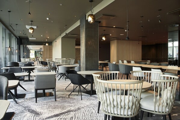 Un restaurante moderno con varias zonas de estar, incluyendo mesas redondas y sillas, y una alfombra estampada.
