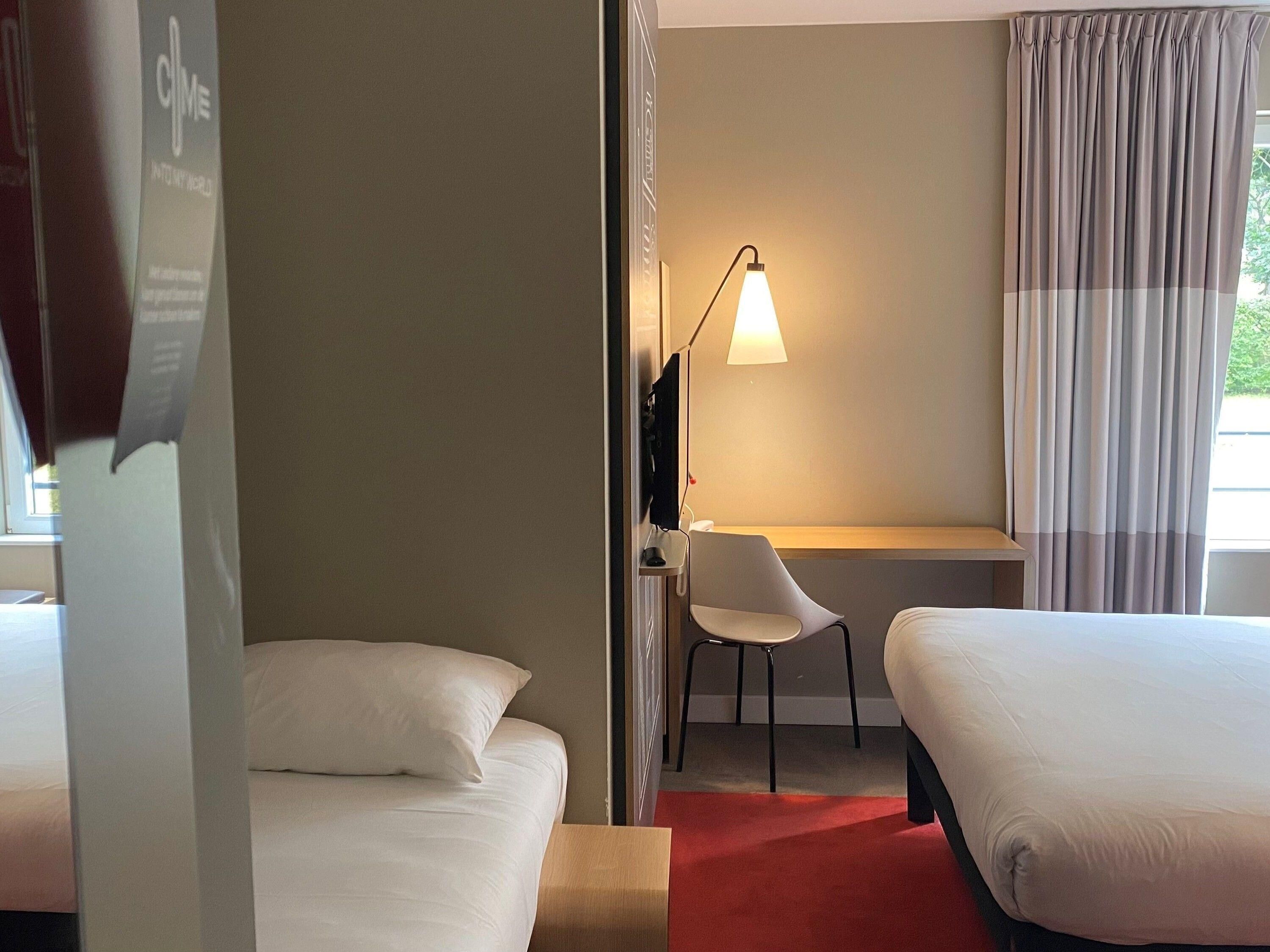 Una habitación de hotel con dos camas, un escritorio, una silla y una lámpara.