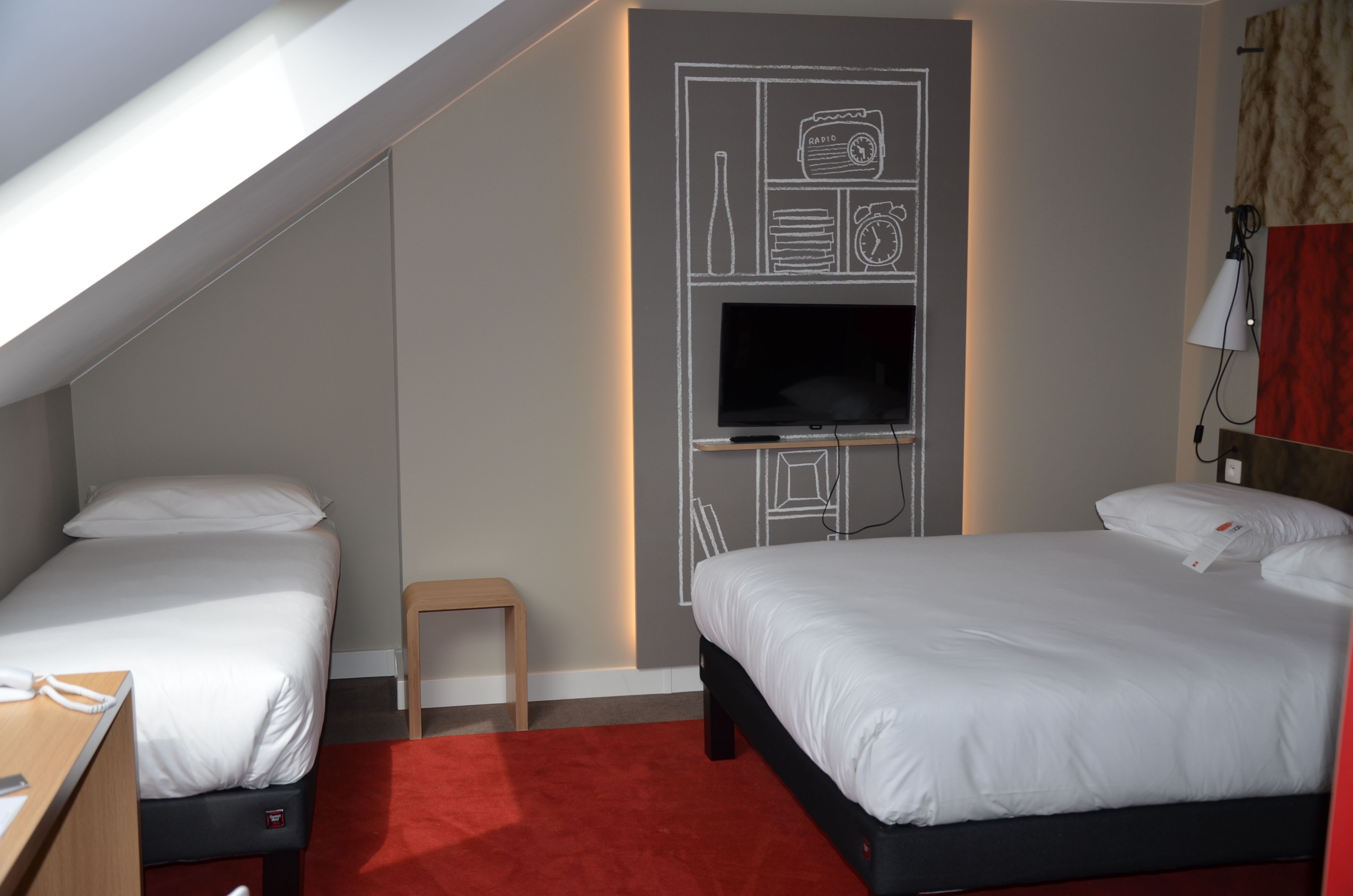 Une chambre d’hôtel avec deux lits, une télévision, une petite table et une moquette rouge.