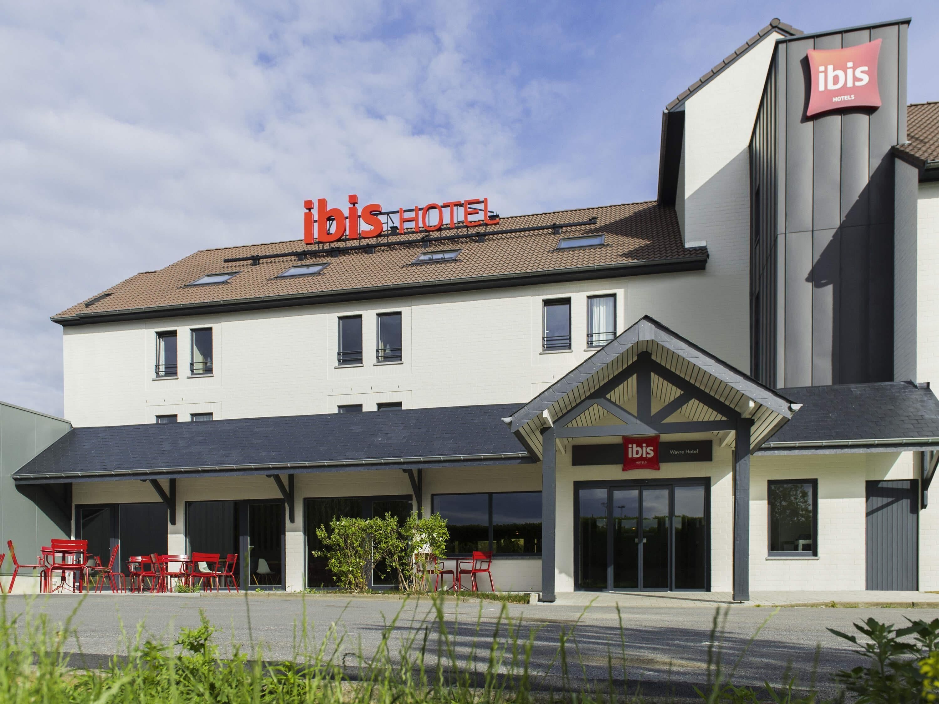 A hotel with a flat roof, multiple windows, and a covered outdoor seating area with red chairs.