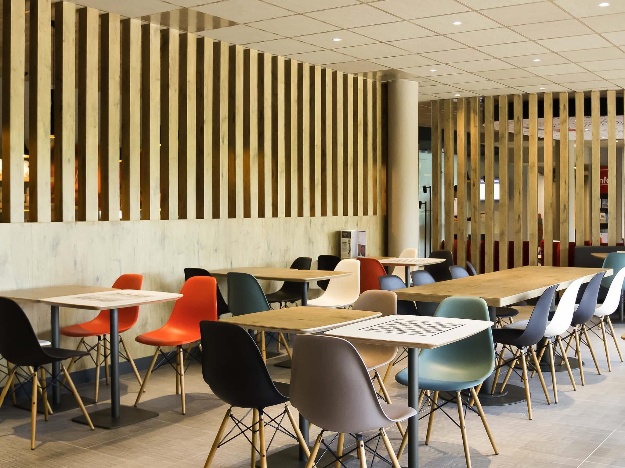 A modern dining area with multiple tables and chairs, wooden slats on the wall, and a tiled floor.