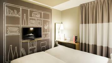 Habitación de hotel con una cama grande, televisión de pantalla plana, escritorio con lámpara y ventana con cortinas.