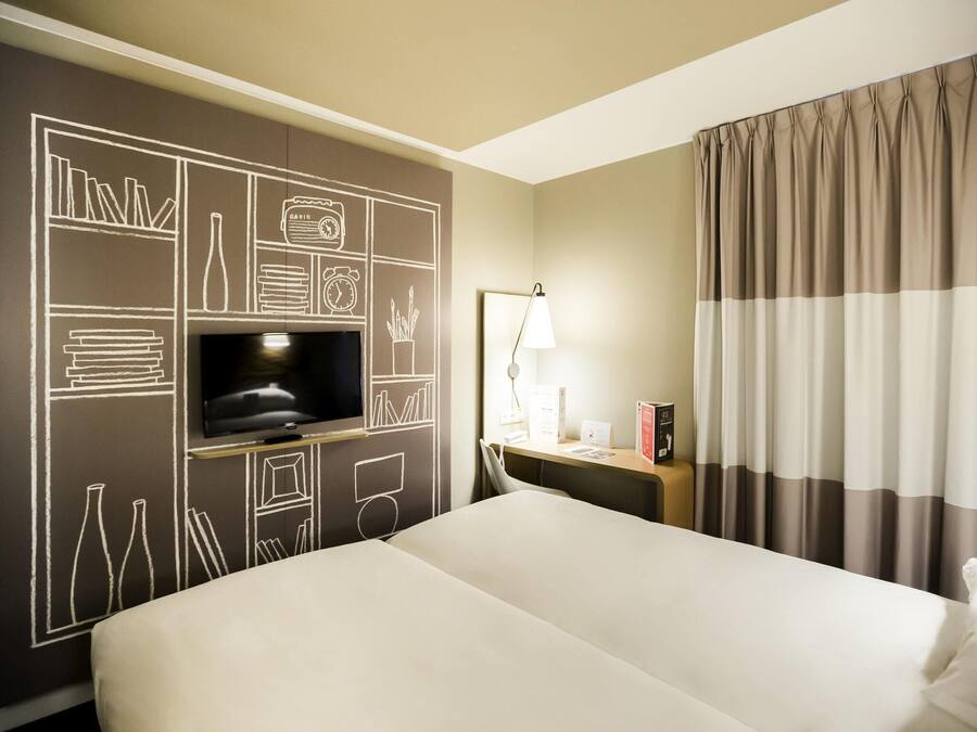 Habitación de hotel con una cama grande, televisión de pantalla plana, escritorio con lámpara y ventana con cortinas.