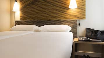 Une chambre d’hôtel avec un lit, deux lampes de chevet, une table de chevet avec une tablette, un sac à main et une paire de chaussures.