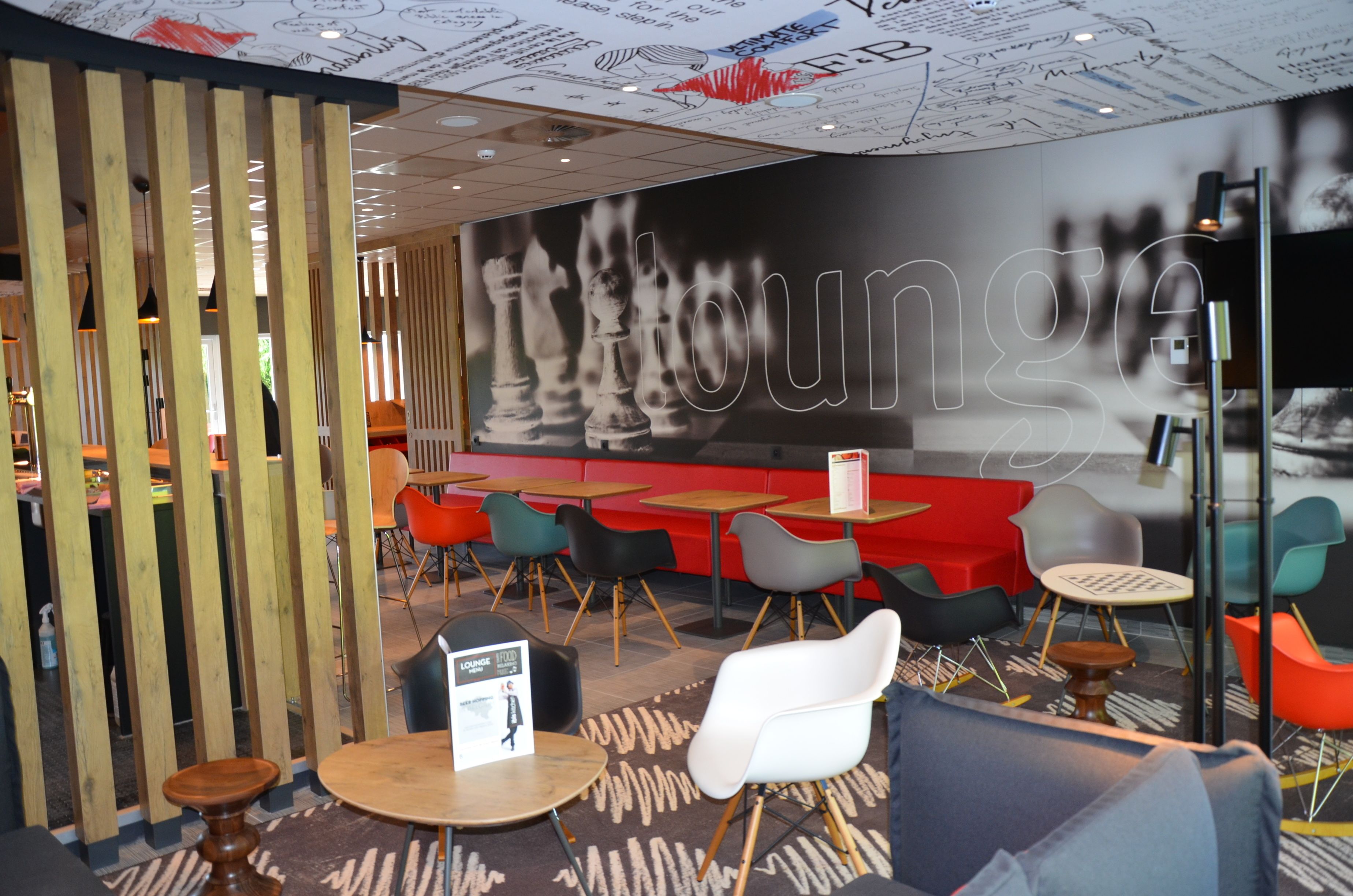 Un espace de détente moderne agrémenté de cloisons en bois, d’une grande fresque représentant un échiquier et de nombreux sièges, notamment des canapés et des fauteuils.