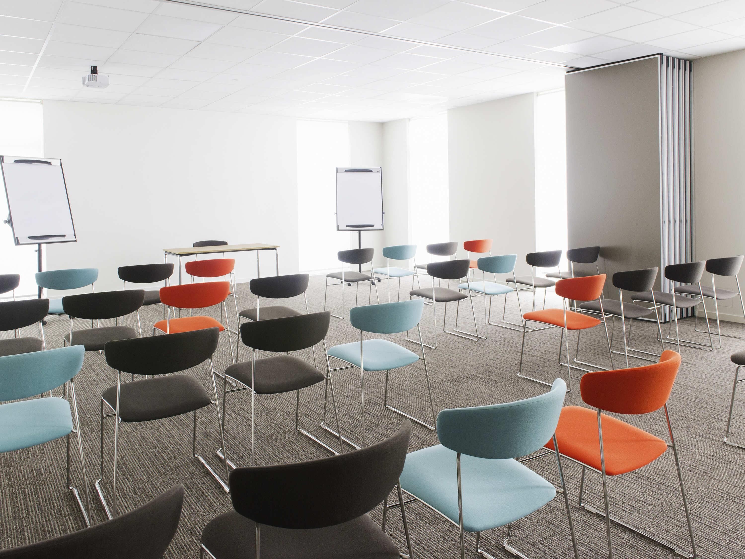Une salle de conférence avec des rangées de chaises, des tableaux blancs et un sol recouvert de moquette.