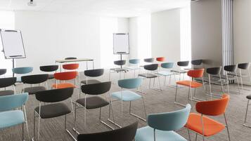 Une salle de conférence avec des rangées de chaises, des tableaux blancs et un sol recouvert de moquette.