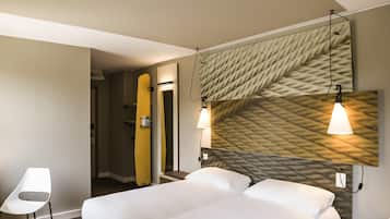 Une chambre d’hôtel avec un lit, des lampes de chevet, une chaise et une planche de surf appuyée contre le mur.