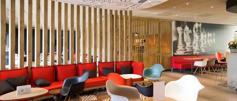 Un área lounge moderna con sofás rojos, sillas negras y blancas, y un mural con temática de ajedrez en la pared.