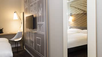A hotel room with a bed, a desk with a chair, a television, and a wall with chalkboard drawings.