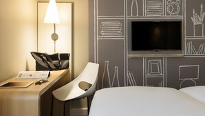 Una habitación de hotel con escritorio, silla, lámpara, televisor y un pared con dibujos estilo pizarra.