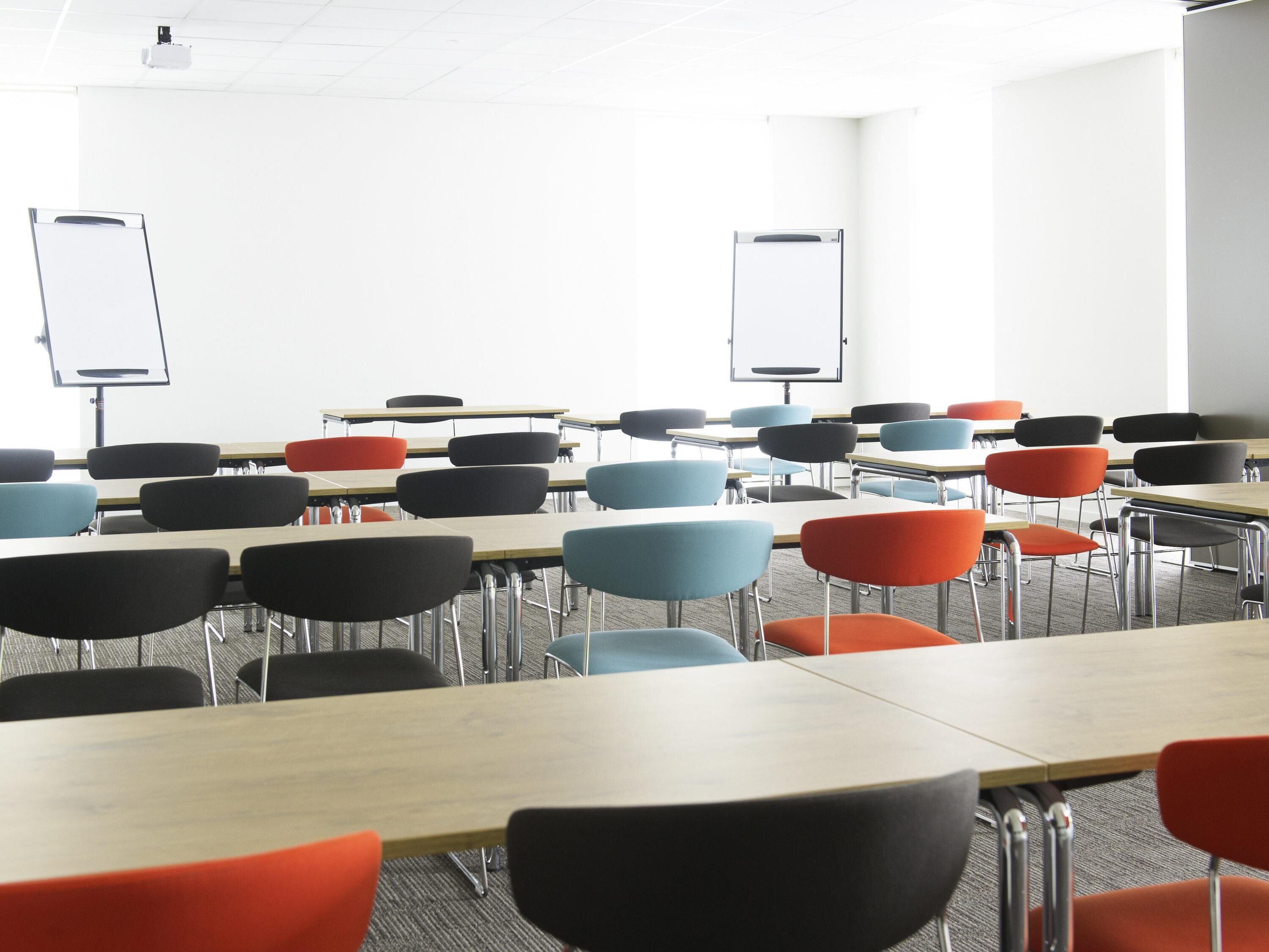 A classroom with rows of desks and chairs, whiteboards, and a projector.