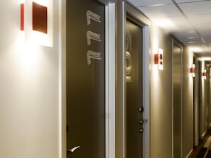 A hotel corridor with doors, each marked with a number and a light switch. - ibis Wavre Brussels East (Wavre)