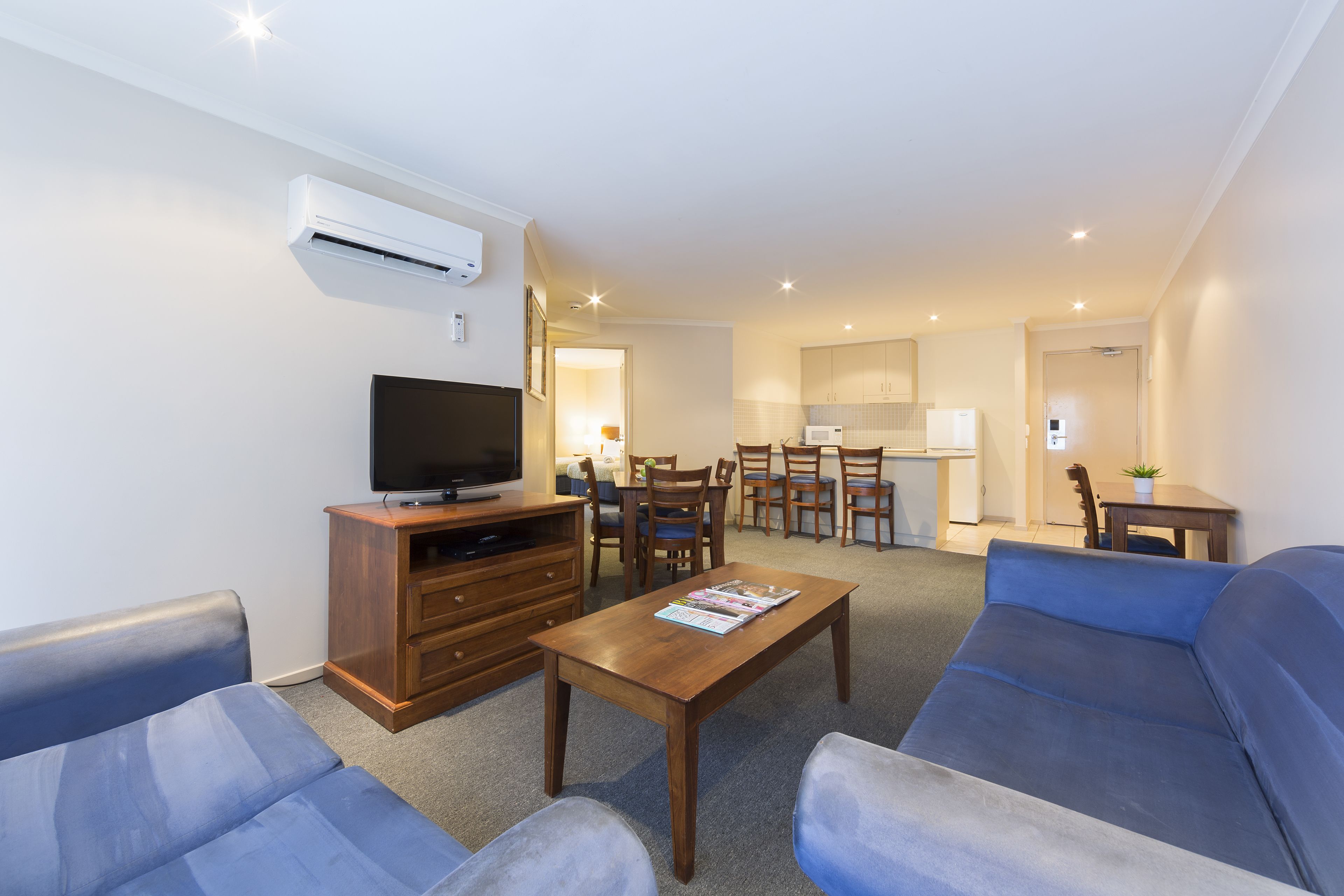 A living room with a sofa, a coffee table, a TV stand, and a dining area with chairs and a table.