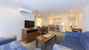 A living room with a sofa, a coffee table, a TV stand, and a dining area with chairs and a table.