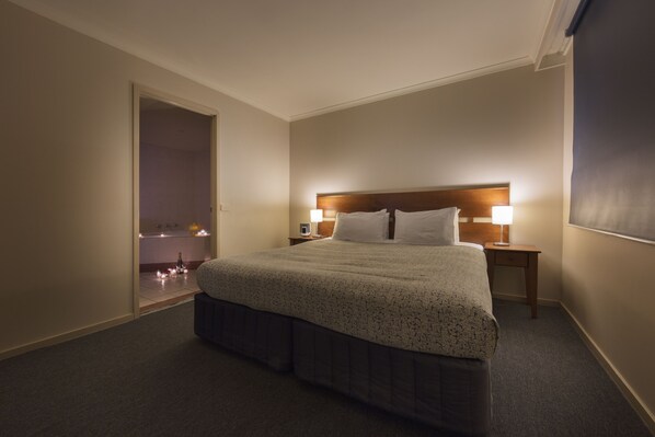 Una habitación de hotel con una cama grande, dos mesitas de noche y una puerta que da a un baño.