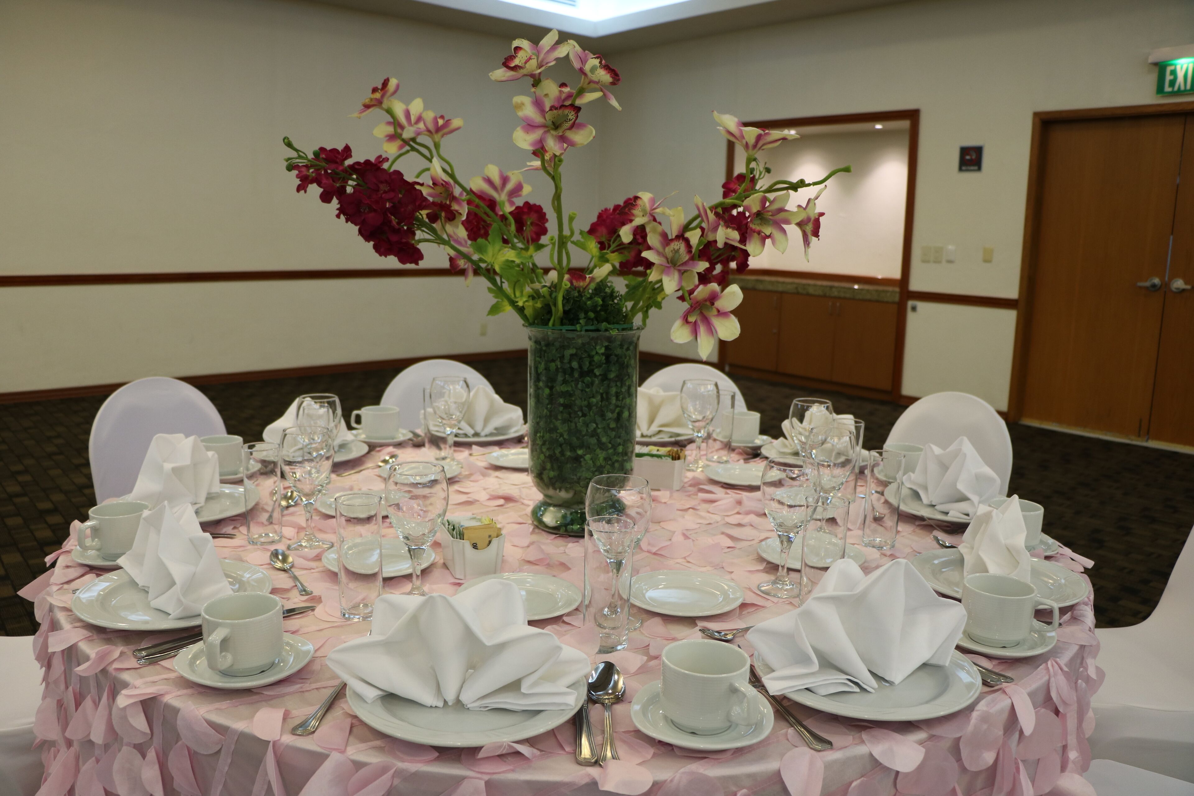 A round table set for a formal event with a floral centerpiece, white tablecloth, and neatly arranged plates, cups, and cutlery.