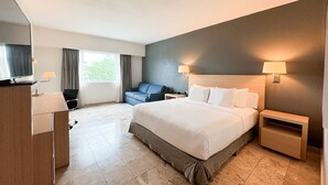 Habitación de hotel con una cama grande, un escritorio, una silla, un televisor y una ventana con cortinas.