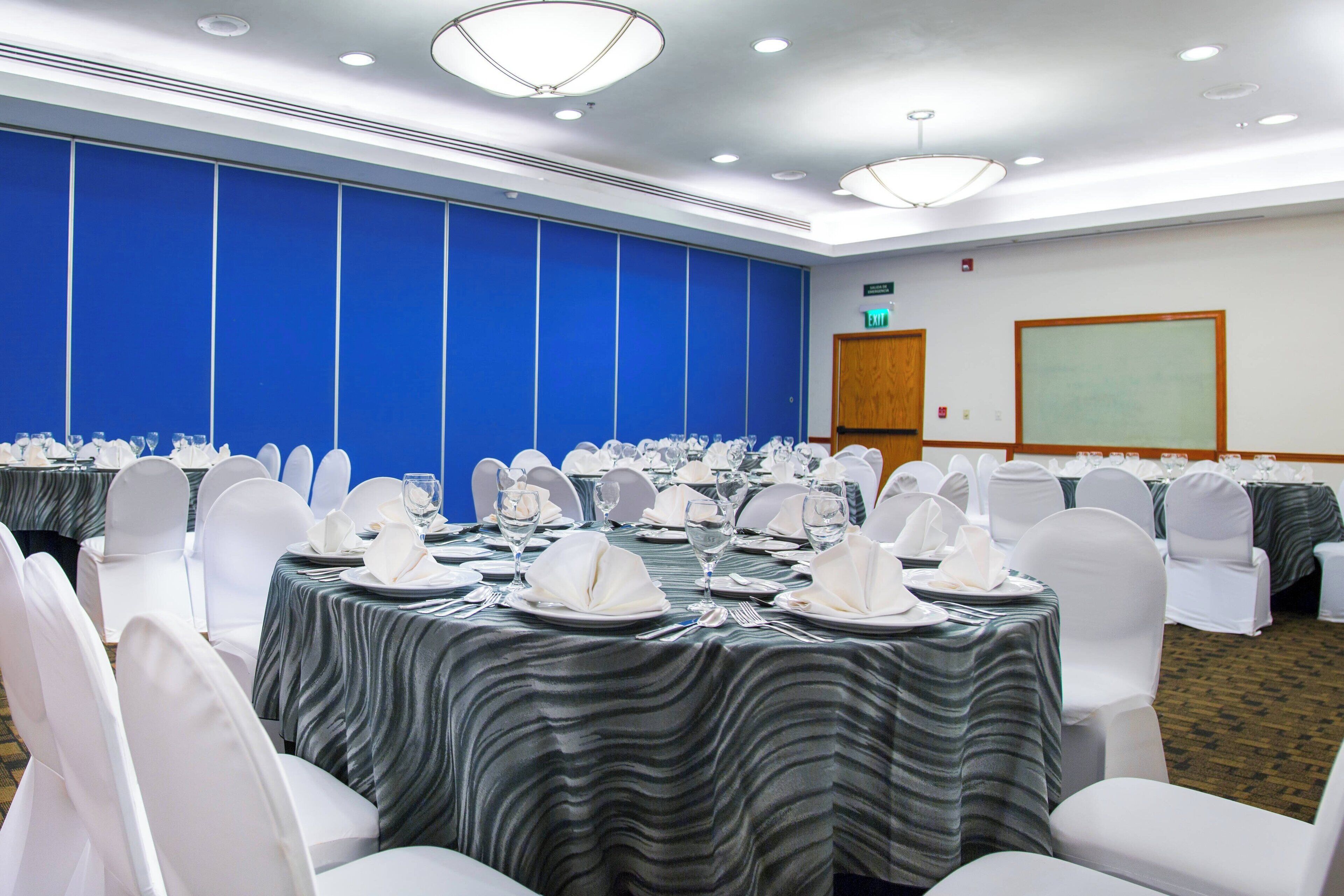 A conference room with tables set for a formal event, featuring white chairs and tablecloths.