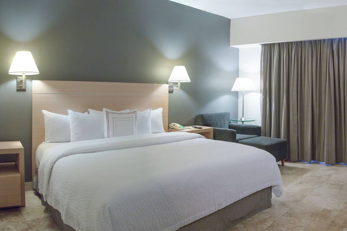 A hotel room with a large bed, two bedside lamps, a chair, and a desk.