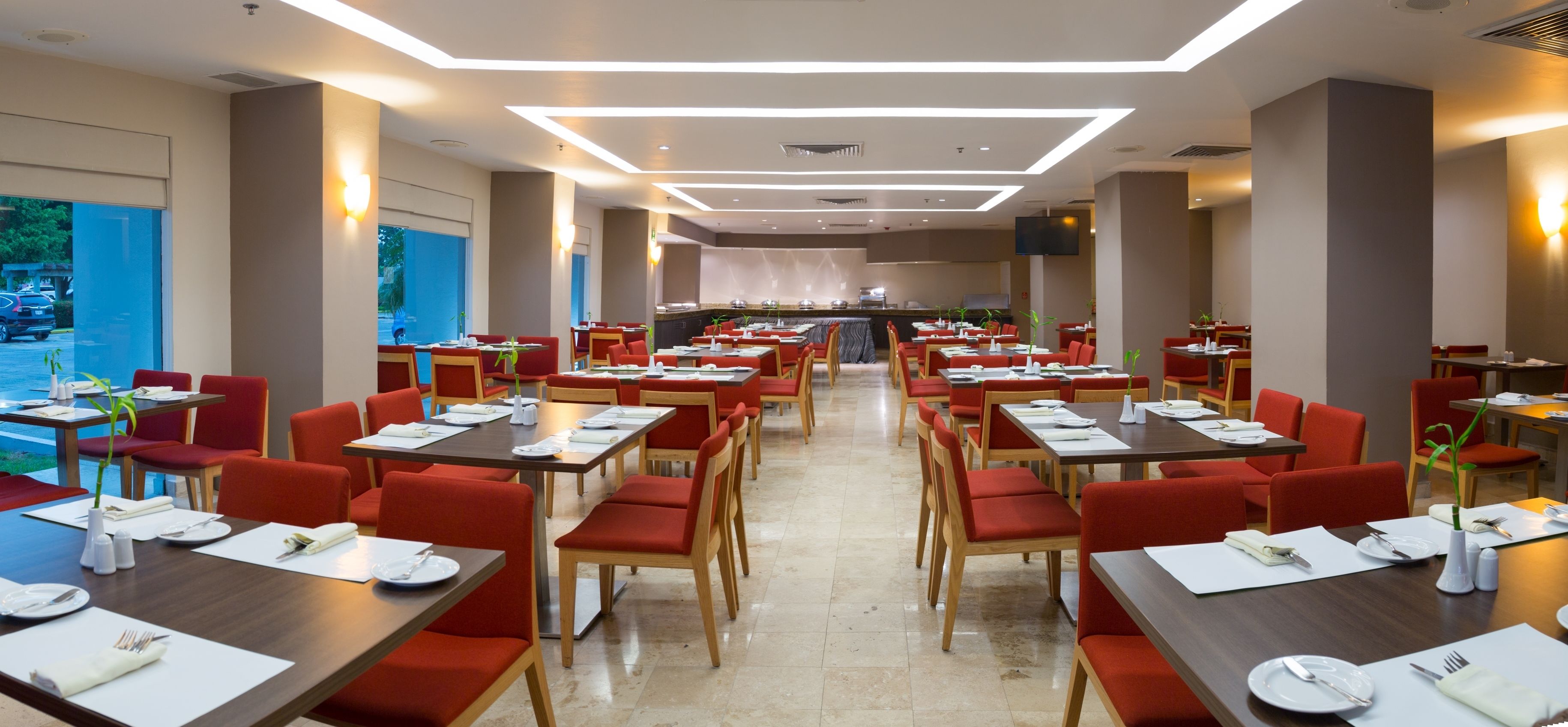 A spacious restaurant with multiple dining tables and chairs, large windows, and a modern ceiling design.