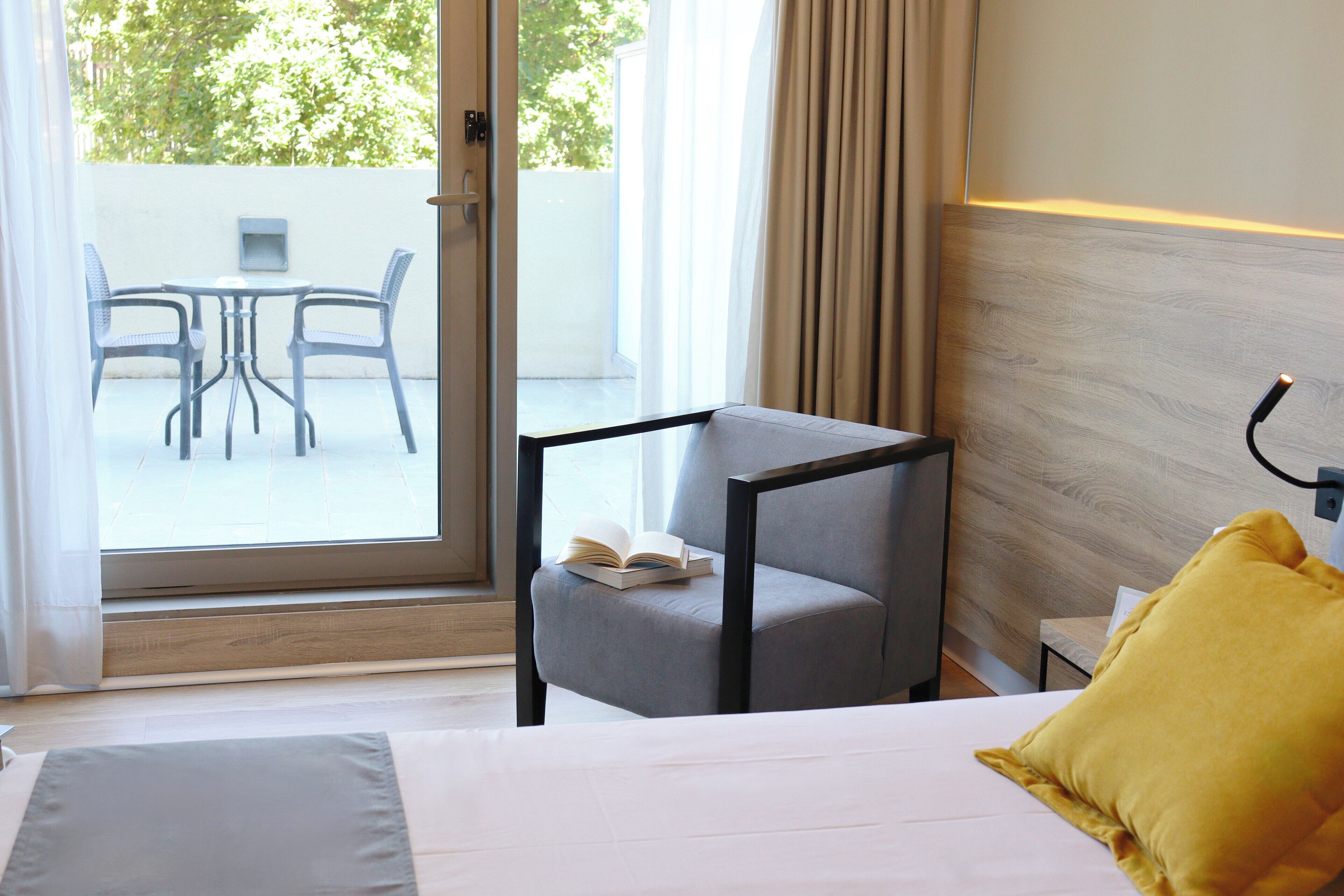 A hotel room with a bed, a chair, a table, and a view of the outside.