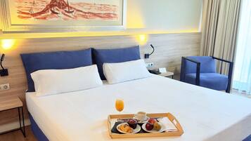 Een hotelkamer met een opgemaakt bed, een nachtkastje met een lamp, een stoel en een dienblad met ontbijtartikelen.