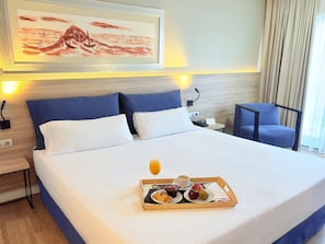 Een hotelkamer met een opgemaakt bed, een nachtkastje met een lamp, een stoel en een dienblad met ontbijtartikelen.
