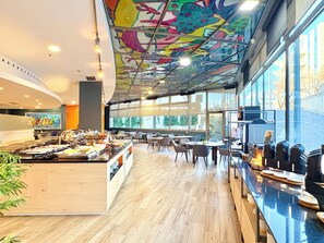 Un restaurant moderne avec une fresque colorée au plafond, un espace buffet et de grandes fenêtres offrant une vue sur l’extérieur.